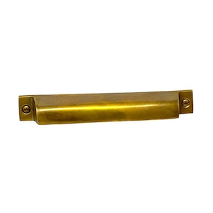 May include: A brass cabinet pull with a rectangular shape and rounded edges. The pull has a brushed finish and two small screws on each end.