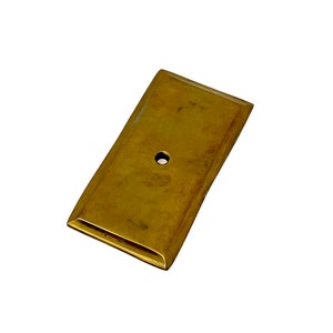 May include: A rectangular brass plate with a single hole in the center. The plate has a slightly rounded edge.