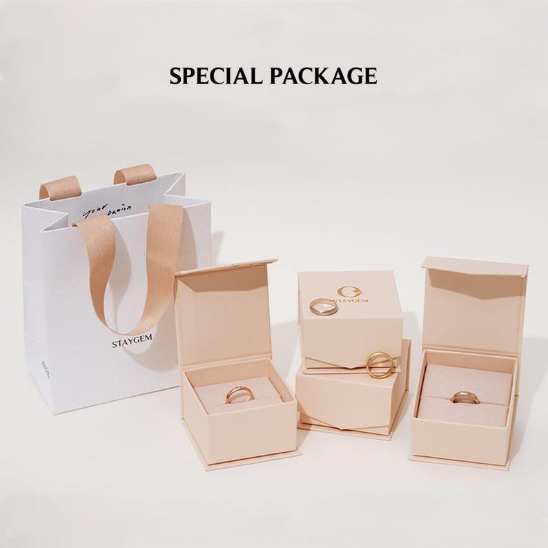 May include: A set of three beige ring boxes with the text "STAYGEM" on the largest box. The boxes are arranged on a white surface. The boxes are for jewellery packaging.