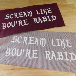 May include: Two rectangular patches with the text "SCREAM LIKE YOU'RE RABID" in white, gothic-style lettering. One patch is burgundy, the other is a light brown with vertical stripes.
