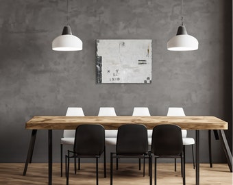 Könnte beinhalten: Ein Esszimmer mit einem großen Holztisch mit schwarzen Metallbeinen, umgeben von schwarzen und weißen Stühlen. Zwei Pendelleuchten beleuchten den Raum. Ein abstraktes Gemälde mit Text hängt an der grauen Wand.