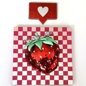 May include: A red and pink checkered background with a red, sparkly strawberry on top. A red heart icon with a white outline is above the strawberry.