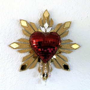 Peut inclure: Décoration murale avec un cœur rouge en mosaïque au centre, entouré d'un motif d'éclat doré. Le cœur est orné de cristaux transparents et l'éclat a des accents dorés et miroir.