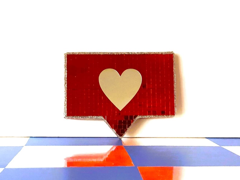 May include: A red and silver glitter heart-shaped button with a white heart in the centre.