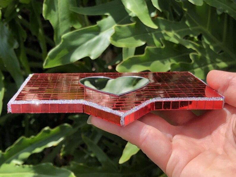 May include: A red mosaic mirror shaped like a heart with a silver glitter border.