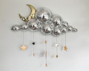 May include: A decorative wall hanging featuring a cloud made of mirrored disco balls, a gold crescent moon, and hanging star accents. The stars are in various metallic finishes. The cloud is approximately 24 inches wide.