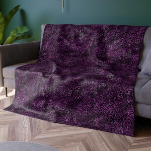 May include: A purple and black leopard print throw blanket draped over a gray couch. The blanket has a soft, plush texture and is perfect for adding a touch of style to any living room.