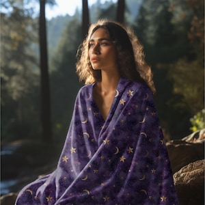 Peut inclure: Une personne enveloppée dans une couverture violet foncé ornée d'un motif céleste de lunes et d'étoiles dorées. La couverture semble douce et confortable, parfaite pour se détendre. Un article unique et attrayant pour la maison.