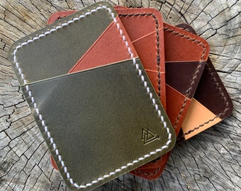 May include: Four leather wallets stacked on top of each other. The top wallet is green with a brown patch and white stitching. The second wallet is brown with a tan patch and white stitching. The third wallet is brown with a black patch and white stitching. The fourth wallet is tan with a brown patch and white stitching. The top wallet has a small triangle logo.