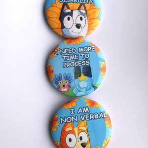 May include: Three round buttons with cartoon dog characters and text. The top button says "I HAVE AN INVISIBLE DISABILITY." The middle button says "I NEED MORE TIME TO PROCESS." The bottom button says "I AM NON VERBAL."