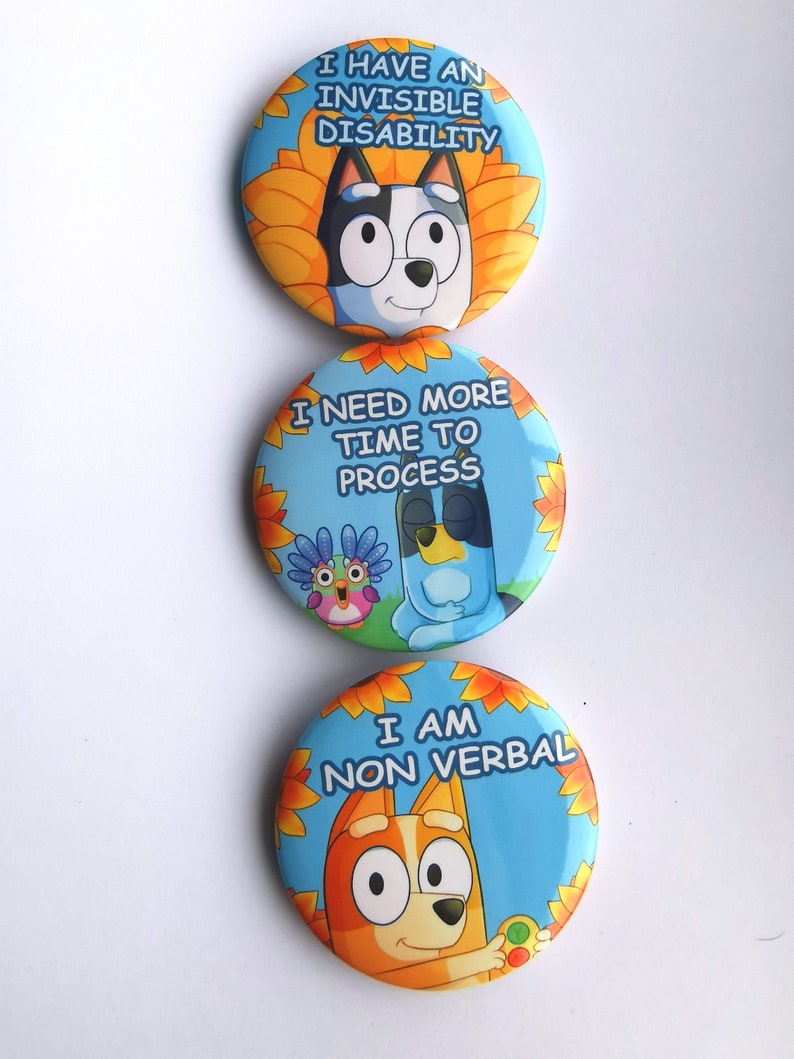 May include: Three round buttons with cartoon dog characters and text. The top button says "I HAVE AN INVISIBLE DISABILITY." The middle button says "I NEED MORE TIME TO PROCESS." The bottom button says "I AM NON VERBAL."