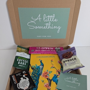 May include: A cardboard gift box containing a yellow crossword book with a peacock illustration, a pack of Taylors coffee bags, a Clipper hot chocolate sachet, a Clipper tea bag, a pack of Border chocolate cookies, and a card reading A little Something.