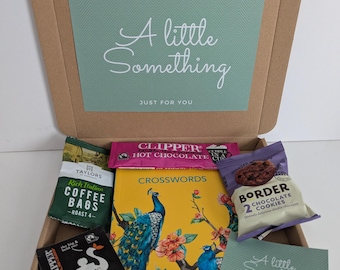 May include: A cardboard gift box containing a yellow crossword book with a peacock illustration, a pack of Taylors coffee bags, a Clipper hot chocolate sachet, a Clipper tea bag, a pack of Border chocolate cookies, and a card reading A little Something.