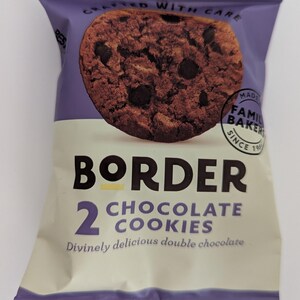 May include: A purple and cream snack package featuring a chocolate chip cookie graphic. The text reads BORDER, 2 CHOCOLATE COOKIES, Divinely delicious double chocolate, CRAFTED WITH CARE, and MADE BY FAMILY BAKERS SINCE 1984 in a circular stamp.
