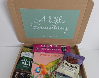 May include: A brown cardboard gift box containing a wordsearch book with a parrot illustration, a packet of Clipper hot chocolate, Taylors coffee bags, Clipper tea, Border chocolate cookies, and a card with the text A little Something.