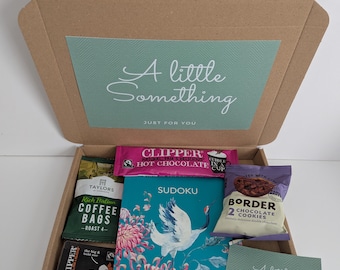 May include: A brown cardboard gift box containing a Sudoku book with a crane and flower illustration, a packet of Clipper hot chocolate, Taylors coffee bags, Clipper tea bags, a pack of Border chocolate cookies, and a small card labeled A little Something.