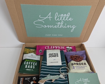 May include: A cardboard gift box containing a pair of dark green striped socks with a Jack & Jones label, a silver fish-shaped keychain, a pack of Taylors coffee bags, two Clipper tea bags, a pack of Border chocolate cookies, and two cards.