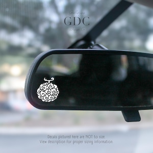 May include: White decal of a stylized fruit, visible in a car's rearview mirror. The decal has a swirling design and a small stem. The image also includes the text "GDC Design Co." and a disclaimer about the decal's size.