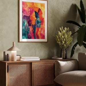 Può includere: Una stampa artistica incorniciata con un design astratto colorato di più profili femminili. L'opera d'arte utilizza una tavolozza di colori vivaci tra cui rosa, arancione, blu e verde acqua. La cornice è di colore marrone caldo.
