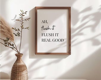 May include: A framed print with the text "AH, flush it, FLUSH IT REAL GOOD" in black script. The frame is a dark wood color. A decorative vase with dried plants sits to the left of the frame.