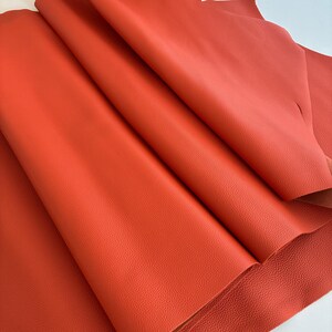 May include: Close-up of a stack of vibrant orange leather sheets. The leather has a textured surface and is folded, revealing the underside. The color is a rich, warm tone, suggesting a high-quality material suitable for various crafting projects.