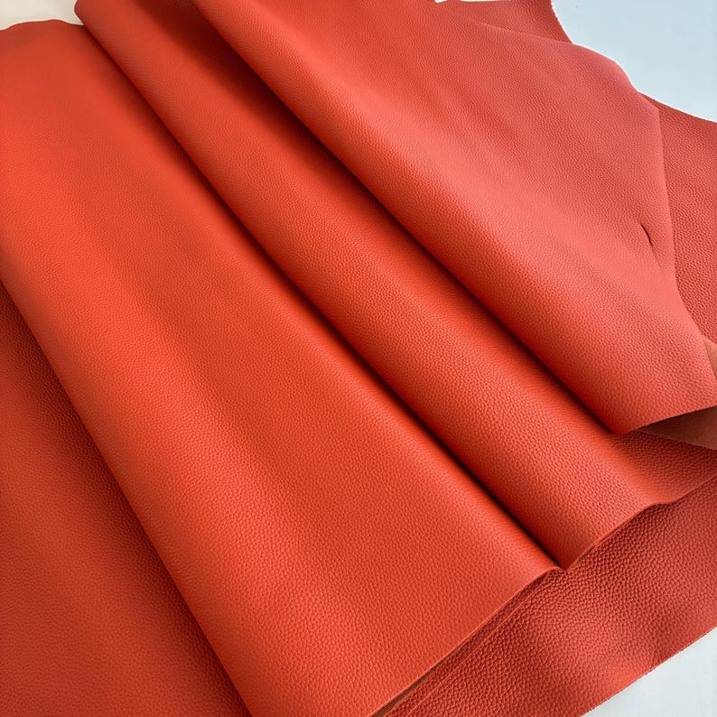 May include: Close-up of a stack of vibrant orange leather sheets. The leather has a textured surface and is folded, revealing the underside. The color is a rich, warm tone, suggesting a high-quality material suitable for various crafting projects.