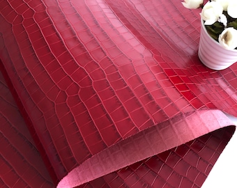 May include: Red crocodile embossed leather fabric. The fabric is folded in half, showing the back side of the material.