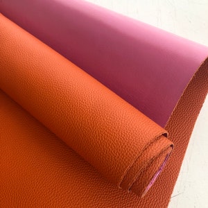 May include: Two rolls of faux leather, one in a burnt orange colour and the other in a dusty rose colour. The orange roll is rolled up and the rose roll is unrolled.