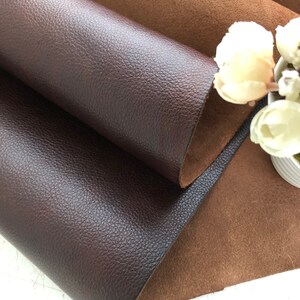 May include: Two pieces of leather fabric, one brown and one dark brown, are folded together. The brown fabric has a smooth texture, while the dark brown fabric has a textured surface.