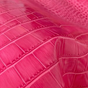 May include: Close-up of a bright pink textured fabric with a crocodile skin pattern.
