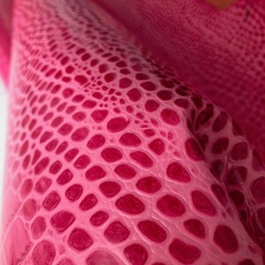May include: Close-up of a pink textured fabric with a repeating pattern of small circles.
