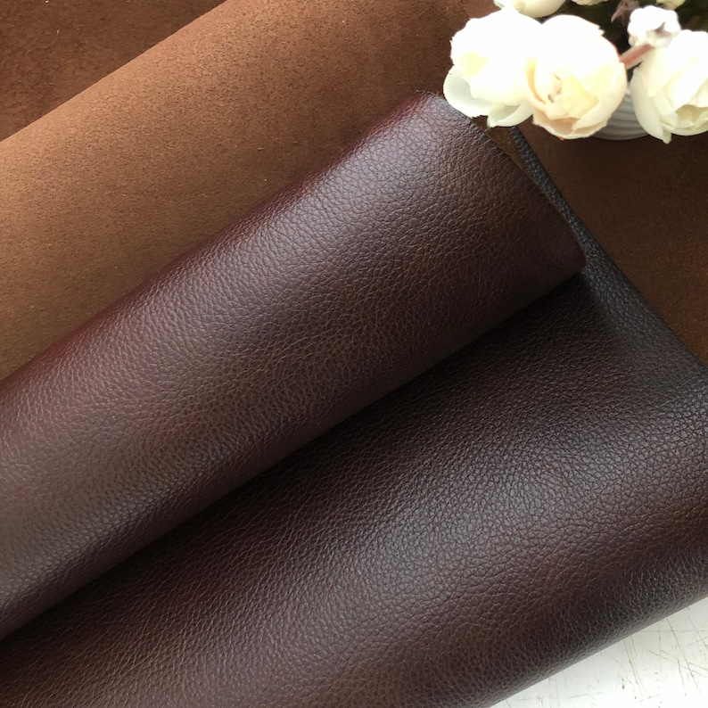 May include: Two pieces of leather fabric, one brown and one dark brown, are folded on top of each other. The dark brown leather has a textured surface.