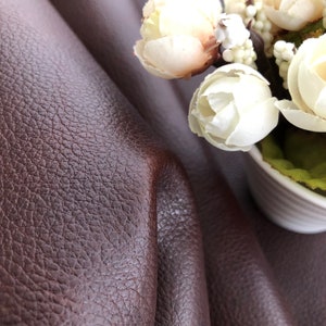 May include: Close-up of a brown leather fabric with a textured surface. A bouquet of white flowers with green leaves is in the background.