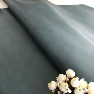 May include: A sheet of light blue wrapping paper with a smooth, matte finish. The paper is folded in half and a small bouquet of white flowers is in the bottom right corner of the image.