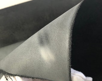 May include: Close-up of a black fabric with a textured surface. The fabric is folded over, revealing a lighter gray side.