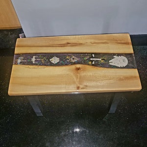 May include: A wooden table with a clear epoxy river running down the centre. The river is filled with glitter and small spaceship figurines. The table has two metal legs.