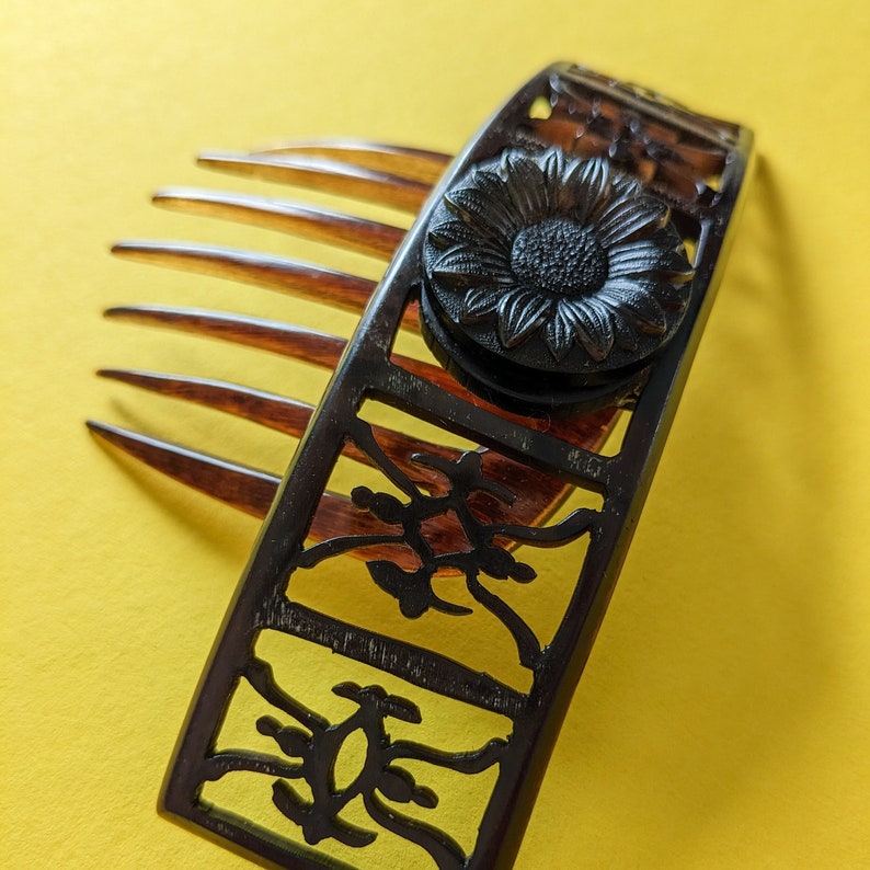 May include: Black hair comb with a decorative floral design and a black flower accent. The comb has a row of teeth on one side and a decorative design on the other.