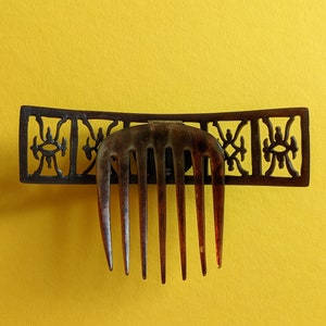 May include: A brown tortoiseshell hair comb with a decorative metal frame. The frame has a geometric design with a repeating pattern.