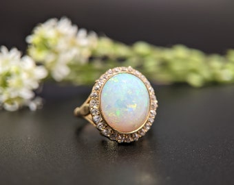 May include: A gold ring with a large oval opal gemstone surrounded by a halo of smaller diamonds.