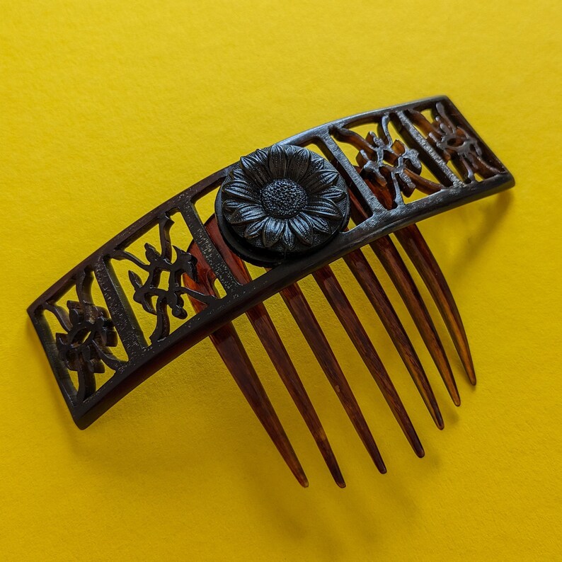 May include: A black hair comb with a decorative floral design and a large black flower accent. The comb has seven teeth.