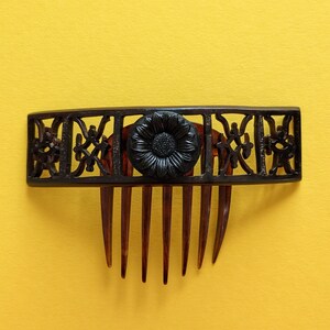 May include: A black plastic hair comb with a decorative floral design and a black flower in the centre.