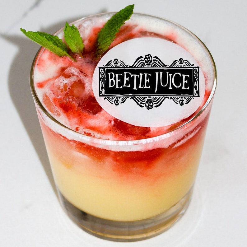 Pode incluir: Um copo de coquetel amarelo e vermelho em camadas com um adesivo redondo branco que diz "Beetle Juice" em letras pretas. A bebida &eacute; decorada com um ramo de hortel&atilde; verde.