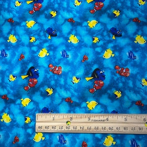 May include: Blue and yellow fabric with a repeating pattern of cartoon fish. The fish include a blue tang, a clownfish, and a yellow fish. The fabric has a light blue background with a watercolor effect.