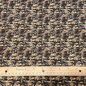 May include: Fabric featuring a repeating pattern of a character from a popular science fiction series. The character is depicted in various poses and expressions, set against a dark background. A ruler is placed at the bottom of the image, measuring up to 12 inches.