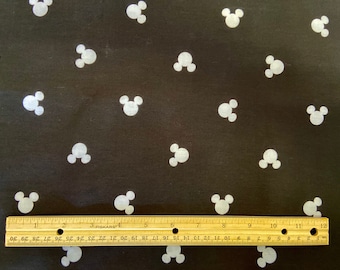 May include: Black fabric with a repeating pattern of white Mickey Mouse head silhouettes. A wooden ruler with inch measurements is placed across the bottom of the fabric. The ruler measures up to 12 inches.