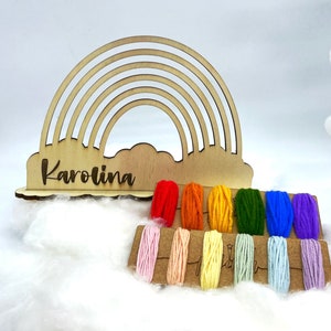 Op de afbeelding: Houten regenboog garen houder met de naam "Karolina" gegraveerd op de basis. De houder wordt geleverd met een set kleurrijke garenklossen in regenboogkleuren.