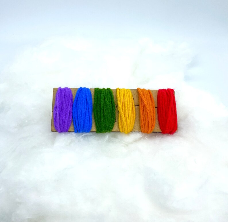 Op de afbeelding: Een set van zes borduurgaren spoelen in regenboogkleuren, waaronder paars, blauw, groen, geel, oranje en rood, gerangschikt op een houten kaart.