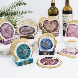 May include: Set of six agate coasters with gold trim and a white base. Each coaster features a different color and pattern, including pink, blue, and green. The coasters are accompanied by a small sign that reads "You are my reason to smile".