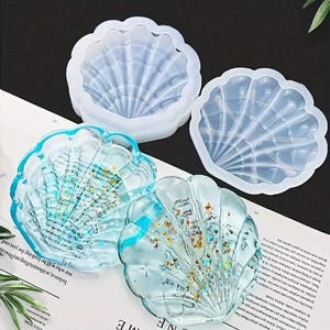 May include: Two clear silicone molds shaped like seashells, and two finished resin castings of the seashells with glitter embedded in the resin.