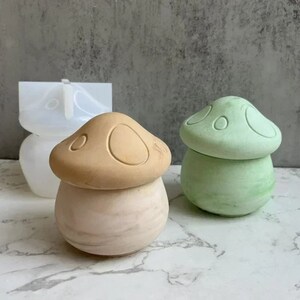 May include: Two mushroom-shaped ceramic containers, one in a light brown color and the other in a light green color. Both containers have a textured surface and a raised design on the top.
